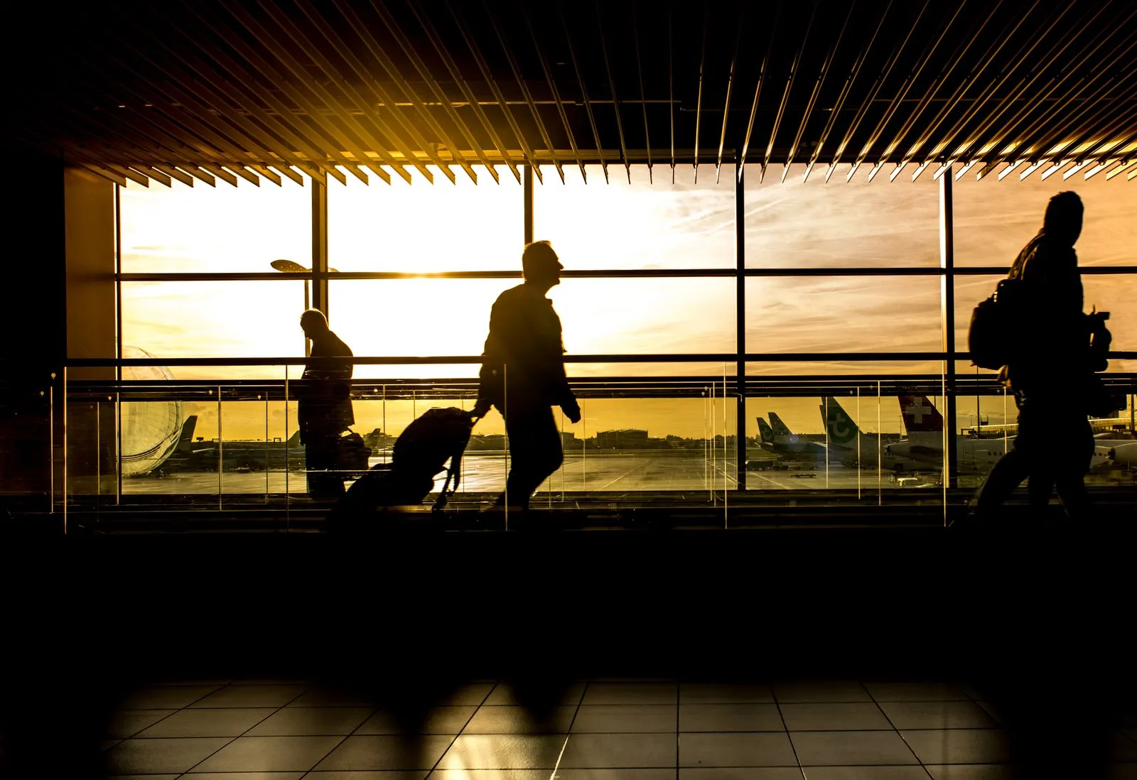 Travellers in an airport arrivals area at sunset with aircraft on the tarmac, where NexDriver drivers meet Linate arrivals with a name sign