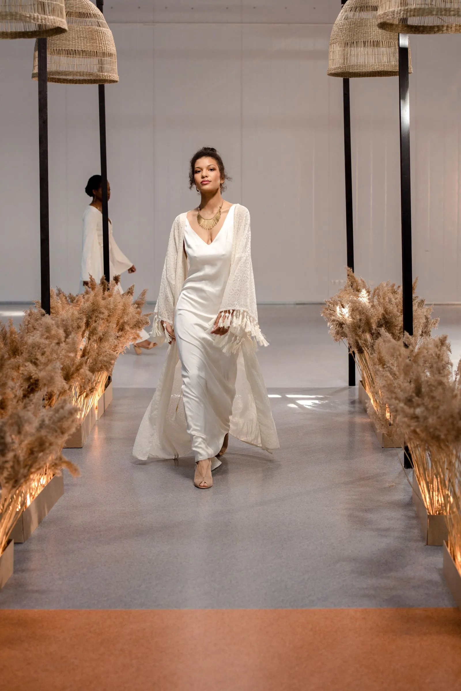 Model walking a runway in a flowing white gown during a fashion show, evoking Milan Fashion Week's runway atmosphere