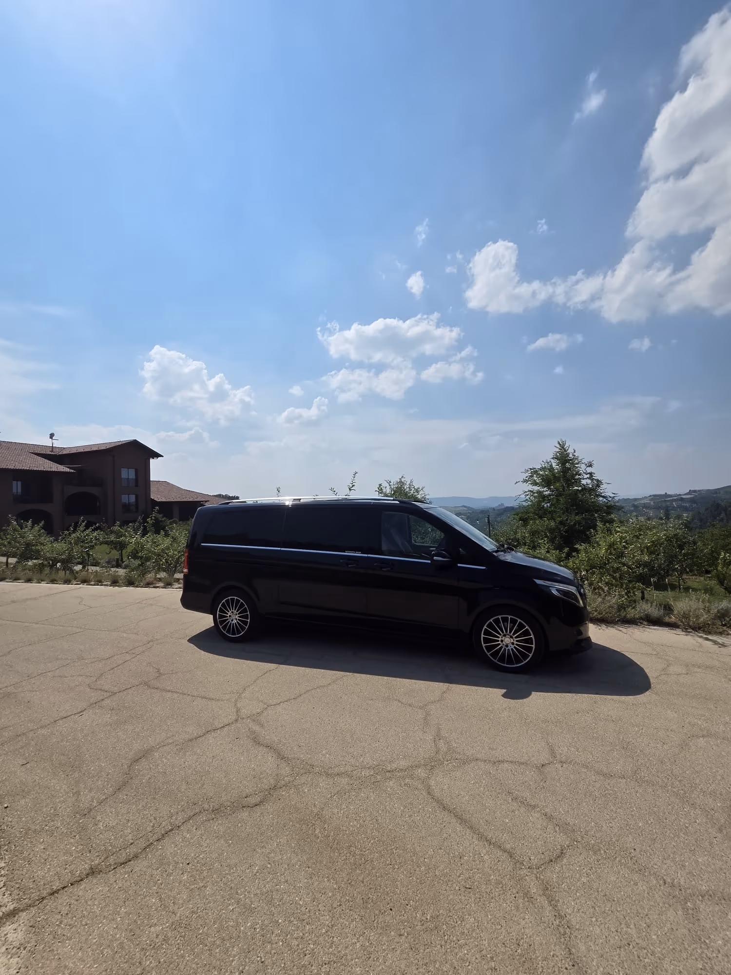 NexDriver's black Mercedes V-Class parked beside a country estate, with rolling hills in the background