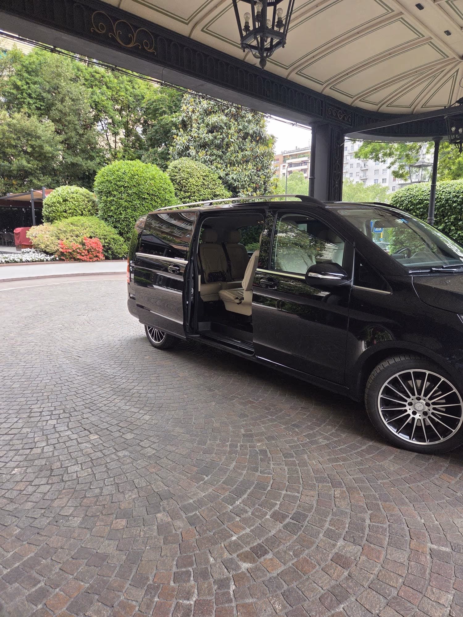 NexDriver Mercedes V-Class with sliding door open at a Milan hotel entrance for a meet-and-greet pickup